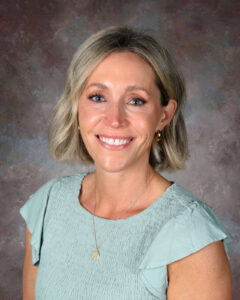 Smiling woman with shoulder-length blonde hair, wearing a light green top and a necklace, against a textured background.