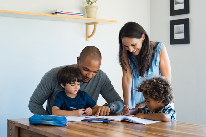 Multiethnic parents helping children with their homework at home. Young father and mother helping sons study at living room. Little boys completing their exercises with the help of dad and mom.