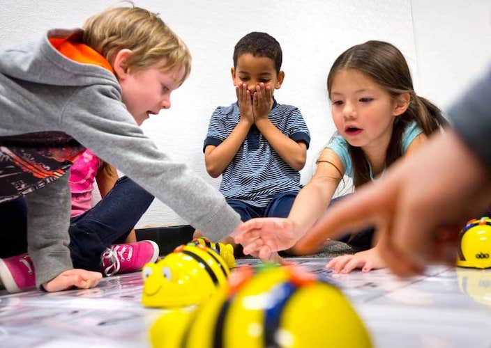 Three preschool age children, a girl and two boys playing with robotic bebots.