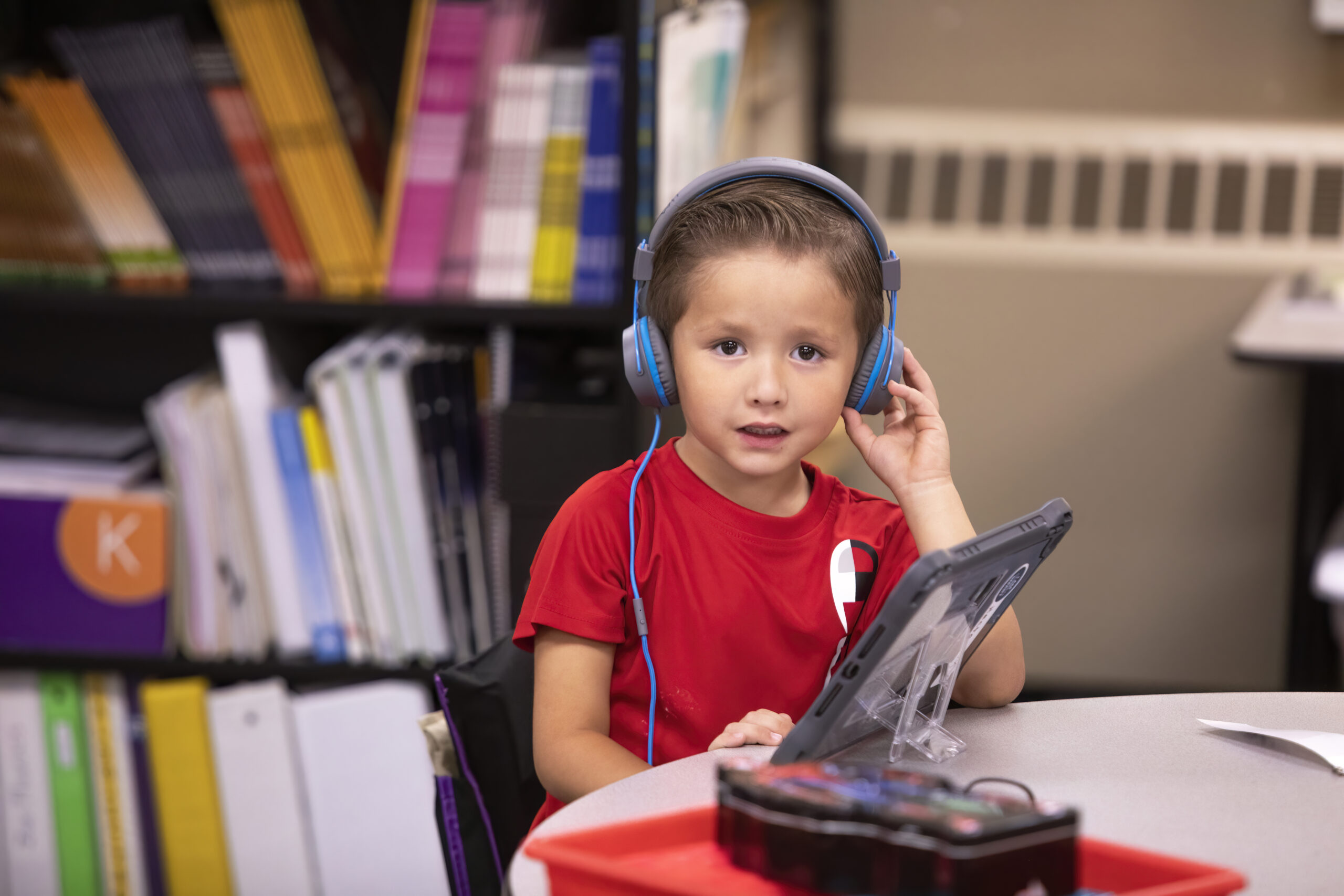 Photograph of a brown haired young boy wearing a red shirt and headphones working on an iPad.